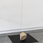 Art gallery installation of stones resting on square silk photographic prints with colour-matched string that hang from the ceiling to the stones.