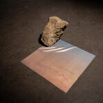 A photographic print on silk rests flat on the gallery ground with a basalt rock on top of it
