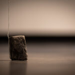 a small piece of basalt sits on the floor with a string hanging from above and tucked underneath it