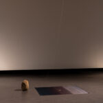 An art installation with a rock and photographic print on silk resting on the floor and a coloured string hanging from the ceiling